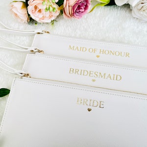 May include: Three white zippered pouches with gold lettering. The pouches are labeled "Bride", "Bridesmaid", and "Maid of Honor".