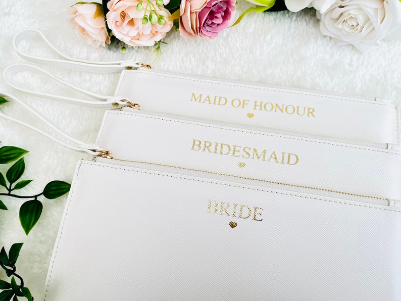 May include: Three white zippered pouches with gold lettering. The pouches are labeled "Bride", "Bridesmaid", and "Maid of Honor".
