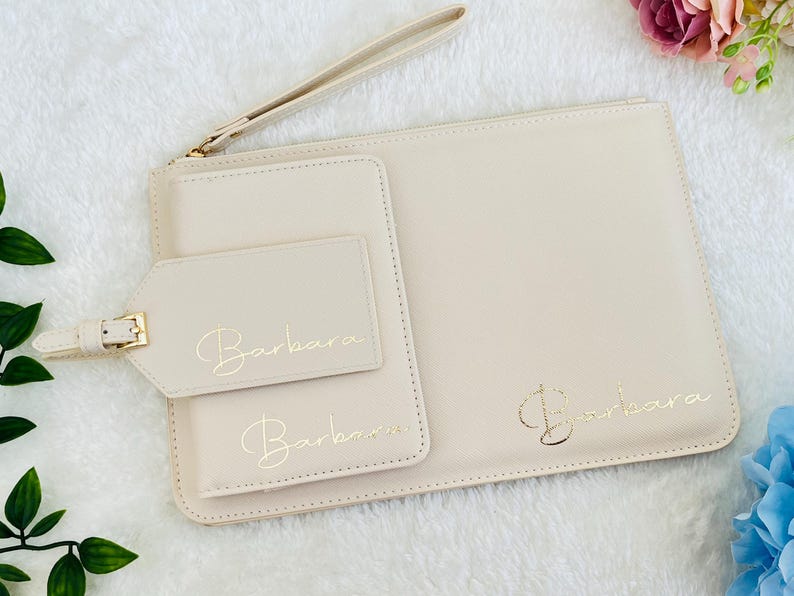 May include: A set of three cream-colored leather pouches with gold lettering. The largest pouch has the name "Barbara" written on it. The medium pouch has the name "Barbara" written on it. The smallest pouch is a luggage tag with the name "Barbara" written on it.