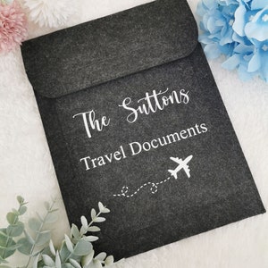May include: Gray felt travel document holder with the text "The Suttons Travel Documents" and a white airplane icon with a dotted line trail.