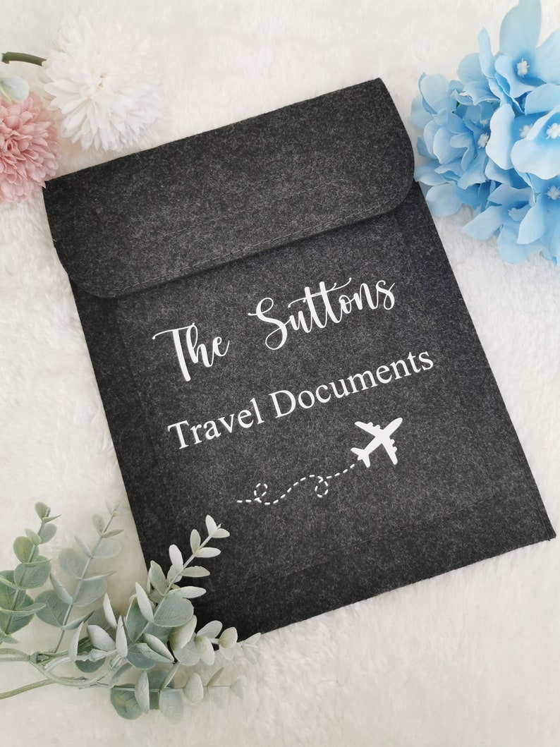 May include: Gray felt travel document holder with the text "The Suttons Travel Documents" and a white airplane icon with a dotted line trail.