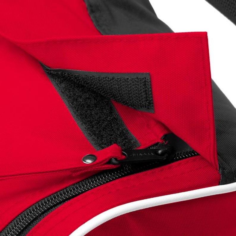 May include: A red and black fabric bag featuring a flap closure secured with a black hook-and-loop fastener strip. The bag includes a black zip with a metal pull tab, a white piping detail along the edge, and a textured black fabric panel.