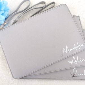 May include: Three gray zippered pouches with silver lettering. The pouches are stacked on top of each other. The top pouch has the name Maddie written on it. The middle pouch has the name Alice written on it. The bottom pouch has the name Leah written on it.
