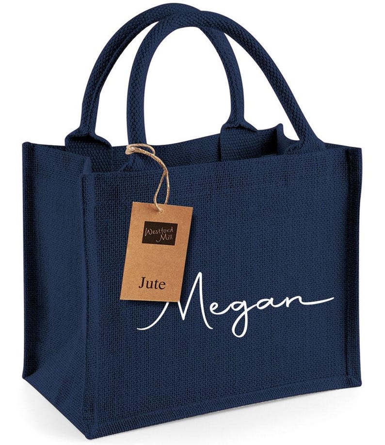 May include: Navy blue jute tote bag with matching handles. The bag features the name "Megan" in white script and a brown tag that reads "Westford Mill" and "Jute".