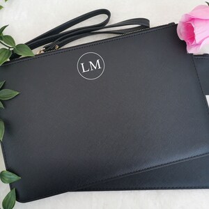 May include: Black leather clutch with a gold zipper and a white circle with the initials "LM" in the center.