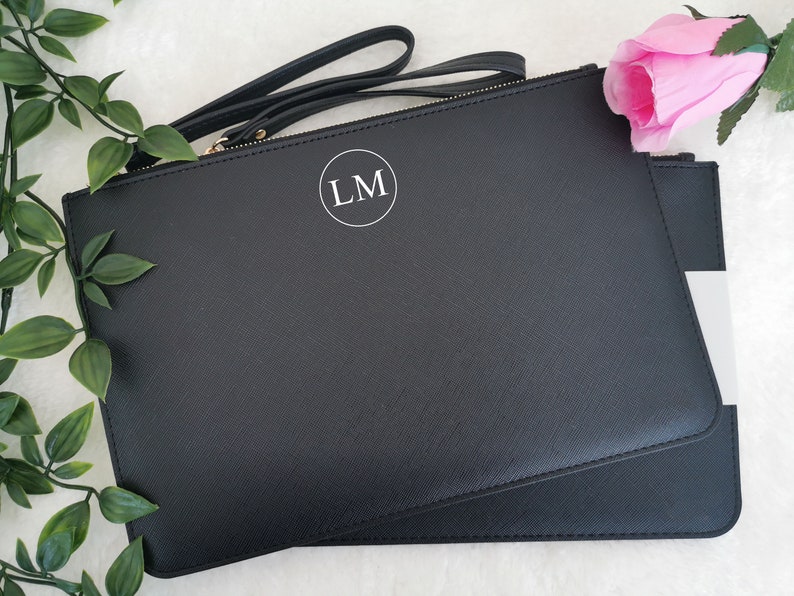 May include: Black leather clutch with a gold zipper and a white circle with the initials "LM" in the center.