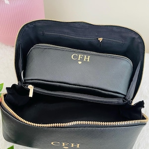 May include: Black cosmetic bag with a gold zipper and the initials "CFH" in gold lettering. The bag is open, revealing a smaller matching pouch inside. The interior is black.