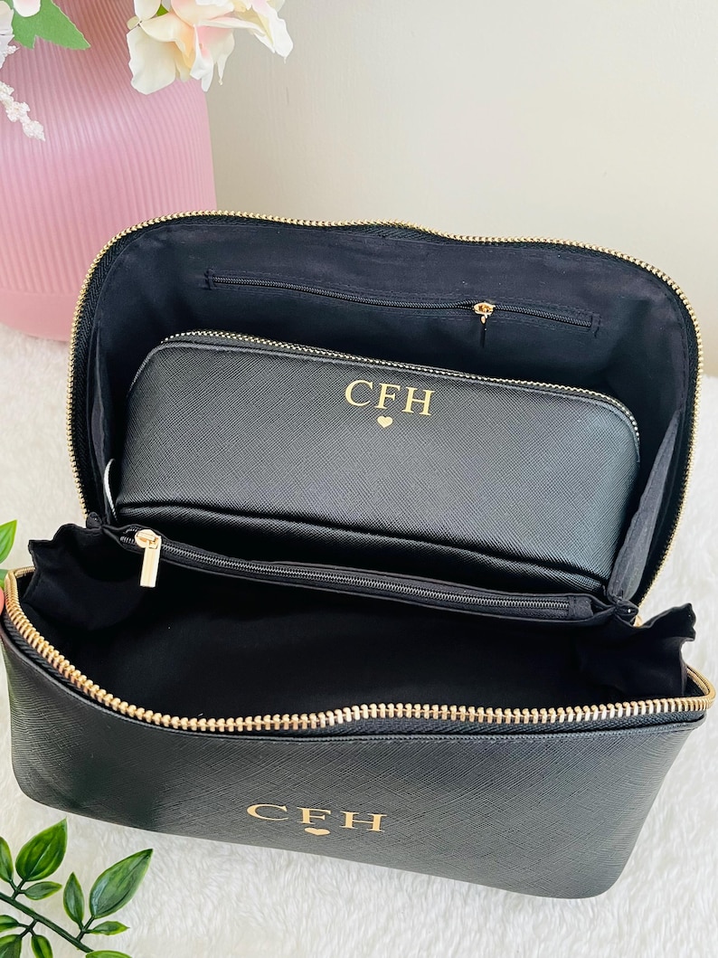 May include: Black cosmetic bag with a gold zipper and the initials "CFH" in gold lettering. The bag is open, revealing a smaller matching pouch inside. The interior is black.