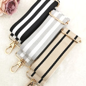 May include: Three striped fabric straps with gold metal clasps. The straps are black and white, grey and white, and beige and black.