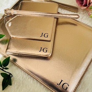 May include: A set of three rose gold travel accessories with the initials "JG" embossed on each piece. The set includes a passport holder, a luggage tag, and a larger pouch.