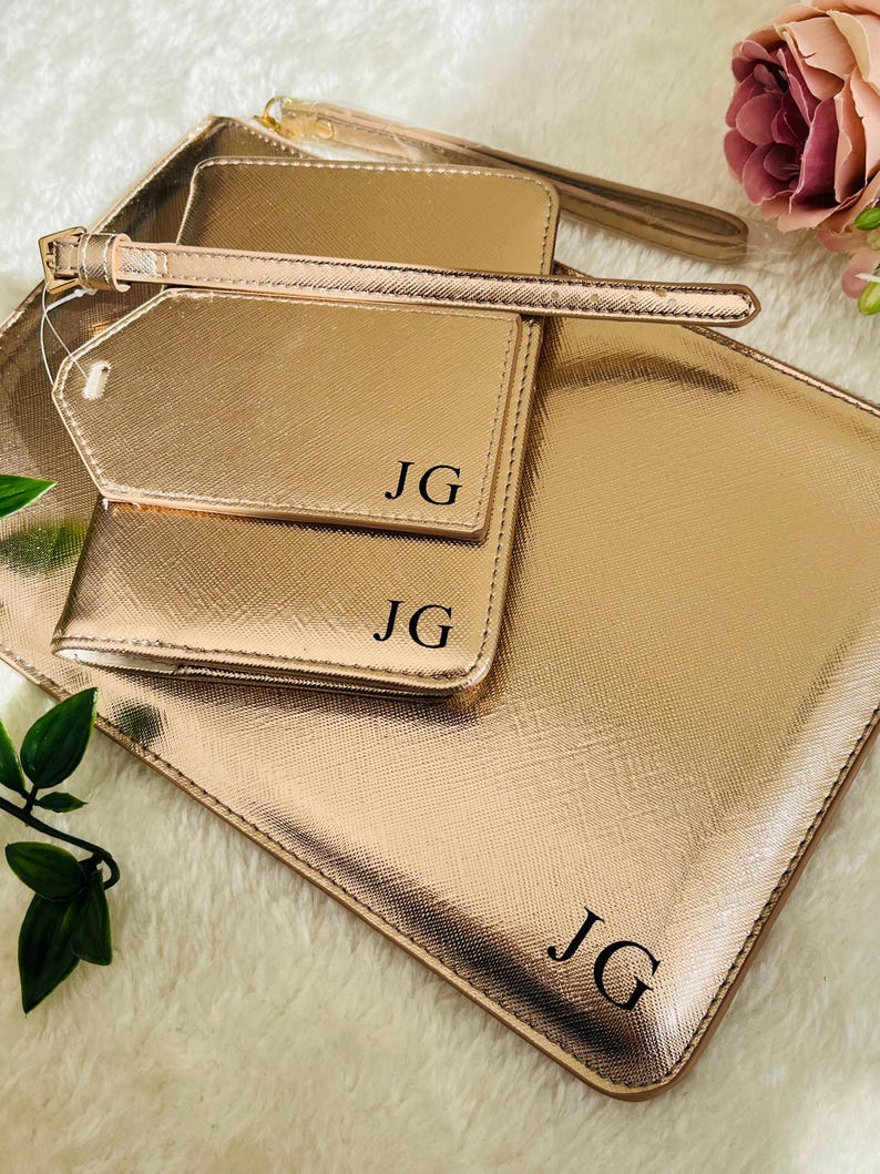 May include: A set of three rose gold travel accessories with the initials "JG" embossed on each piece. The set includes a passport holder, a luggage tag, and a larger pouch.