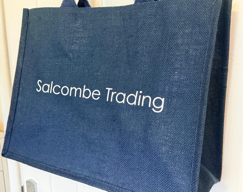 May include: A navy blue tote bag with the text "Salcombe Trading" in white. The bag has two handles and appears to be made of a textured fabric. The bag is rectangular and has a simple design.