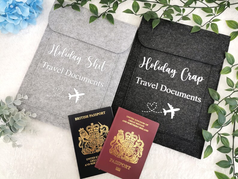 May include: Two gray felt travel document holders with the text "Holiday Shit Travel Documents" and "Holiday Crap Travel Documents" in white. Each holder features a white airplane icon with a heart-shaped trail.