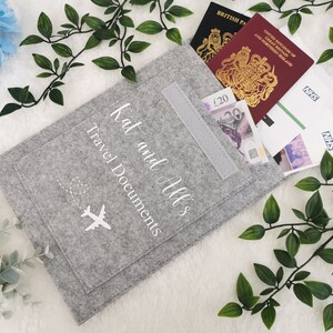 May include: Gray felt travel document holder with a pocket and a white airplane graphic. The text "Kat and All's Travel Documents" is embroidered on the front.