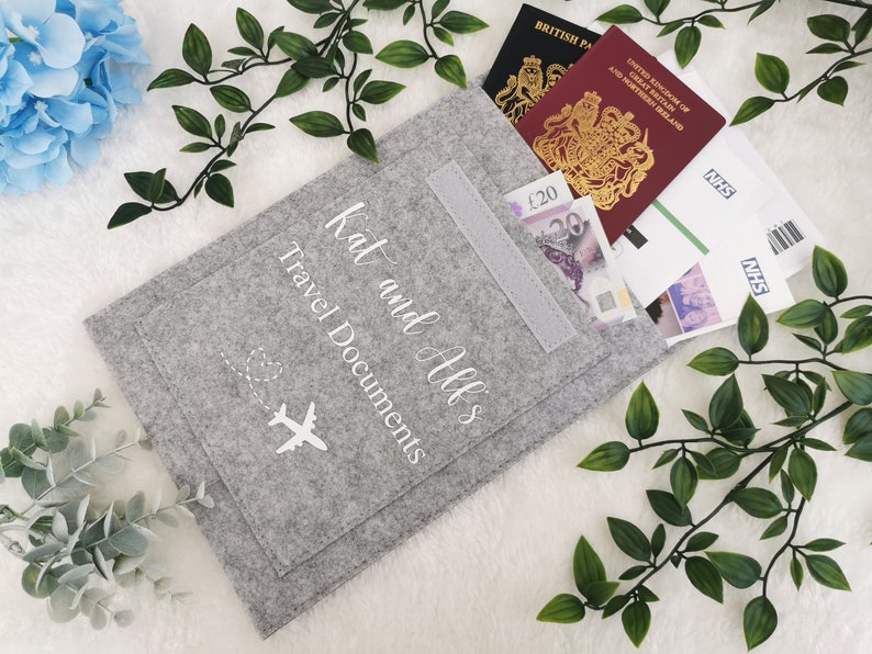 May include: Gray felt travel document holder with a pocket and a white airplane graphic. The text "Kat and All's Travel Documents" is embroidered on the front.