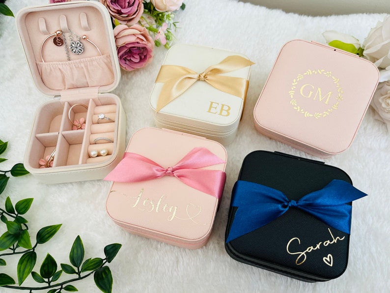 K&ouml;nnte beinhalten: Vier verschiedene Schmuckk&auml;stchen mit personalisierten Namen und Initialen. Die K&auml;stchen sind alle quadratisch und haben ein Samt-Innenfutter. Die K&auml;stchen sind rosa, wei&szlig;, schwarz und cremefarben.