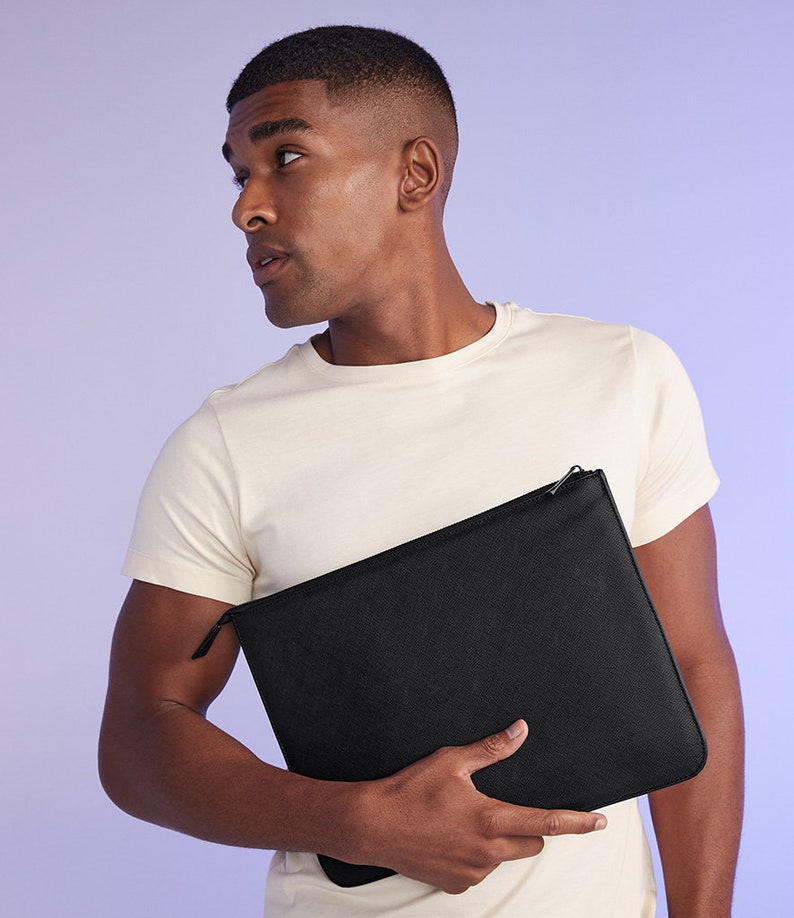 May include: A black zippered pouch with a smooth, textured surface. The pouch is held by a person wearing a white t-shirt.