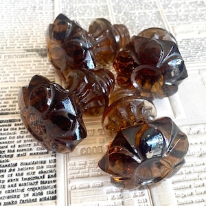 May include: A collection of brown, decorative glass knobs with a floral design. These vintage-style knobs are made of a translucent, amber-colored glass and are ideal for furniture restoration or craft projects.