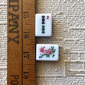 May include: Two white ceramic tiles with black and green markings. The first tile has the number "2" in red and the second tile has the number "3" in red and a floral design with a red bird.