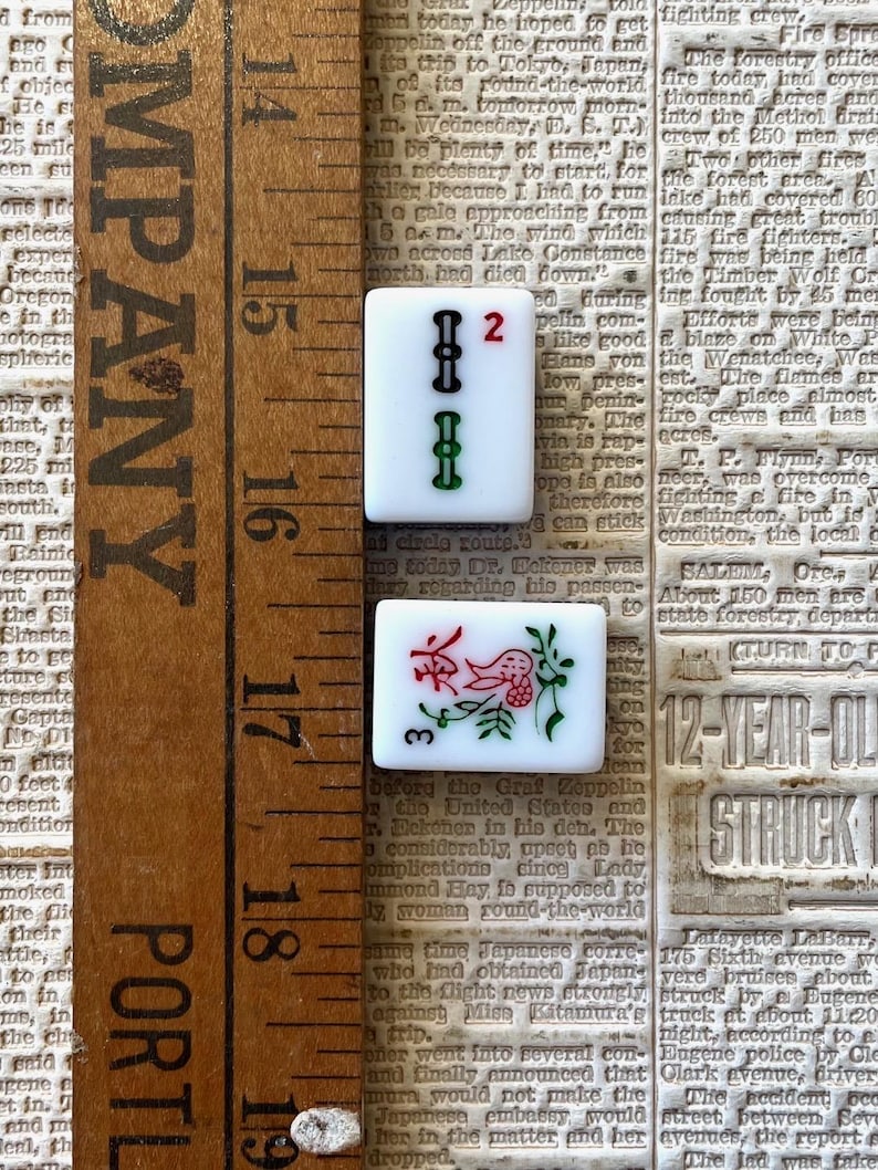 May include: Two white ceramic tiles with black and green markings. The first tile has the number "2" in red and the second tile has the number "3" in red and a floral design with a red bird.
