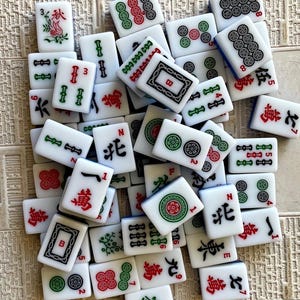 May include: A collection of white and blue mahjong tiles with various Chinese characters and symbols. The tiles are arranged in a random pattern on a beige surface.