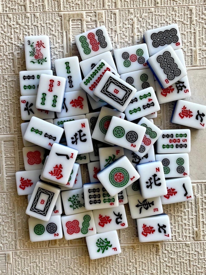 May include: A collection of white and blue mahjong tiles with various Chinese characters and symbols. The tiles are arranged in a random pattern on a beige surface.