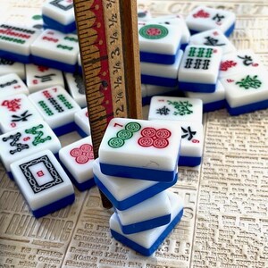 May include: A stack of four blue and white mahjong tiles with green and red symbols. The tiles are stacked on top of a wooden ruler with markings in inches.
