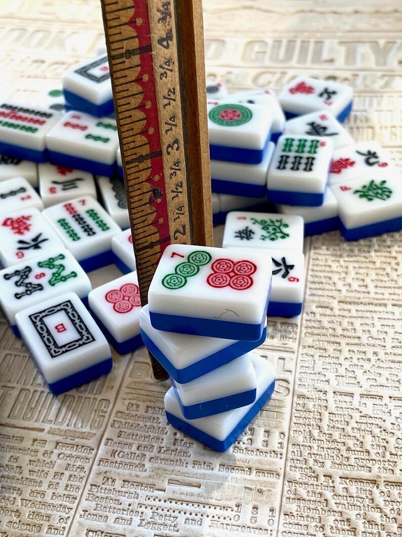 May include: A stack of four blue and white mahjong tiles with green and red symbols. The tiles are stacked on top of a wooden ruler with markings in inches.