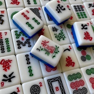 May include: A close-up of a set of mahjong tiles, with various symbols and numbers. The tiles are white with blue and green accents. Some of the tiles have Chinese characters on them.