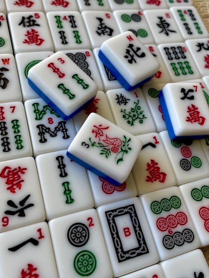 May include: A close-up of a set of mahjong tiles, with various symbols and numbers. The tiles are white with blue and green accents. Some of the tiles have Chinese characters on them.