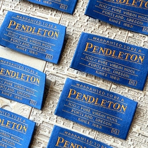 May include: A collection of blue fabric labels with gold embroidered text. Each label reads "PENDLETON" and "100% Pure Virgin Wool, Portland, Oregon, Since 1863." The labels are rectangular with rounded corners and the size "XL".