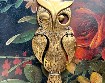 May include: A gold owl pendant necklace with a detailed design and large, round eyes. The owl is hanging from a thick gold chain.