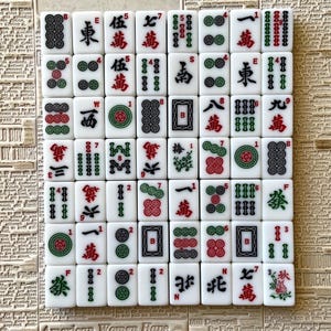 May include: A set of 36 white mahjong tiles with green and red accents. The tiles feature Chinese characters and symbols, including bamboo, circles, and dragons. The tiles are arranged in a grid pattern on a white surface.