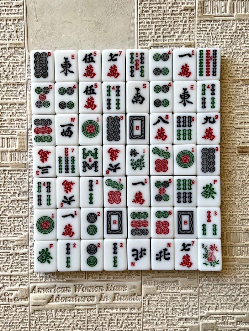 May include: A set of 36 white mahjong tiles with green and red accents. The tiles feature Chinese characters and symbols, including bamboo, circles, and dragons. The tiles are arranged in a grid pattern on a white surface.