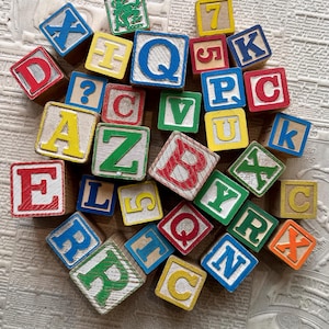 May include: A collection of wooden alphabet and number blocks featuring various letters and digits in red, blue, green, and yellow. Each block displays a single character, including uppercase and lowercase letters, numbers, and a green graphic of a figure.
