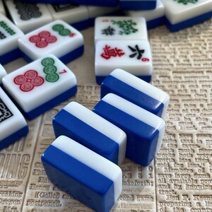 May include: Three blue and white mahjong tiles with white and red Chinese characters. The tiles are stacked on top of each other.