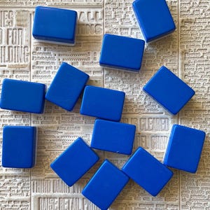 May include: A collection of 10 blue rectangular tiles with white edges. The tiles are arranged in a random pattern on a newspaper background.