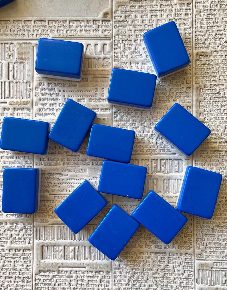 May include: A collection of 10 blue rectangular tiles with white edges. The tiles are arranged in a random pattern on a newspaper background.
