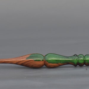 K&ouml;nnte beinhalten: Ein H&auml;kelnadel aus Holz mit einem gr&uuml;nen Harzgrif. Die Nadel ist spitz zulaufend und hat eine glatte Oberfl&auml;che.