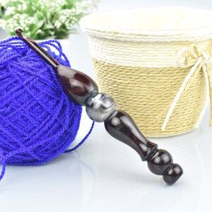 May include: A close-up of a blue yarn ball, a wooden crochet hook with a silver accent, and a woven basket with a white ribbon.