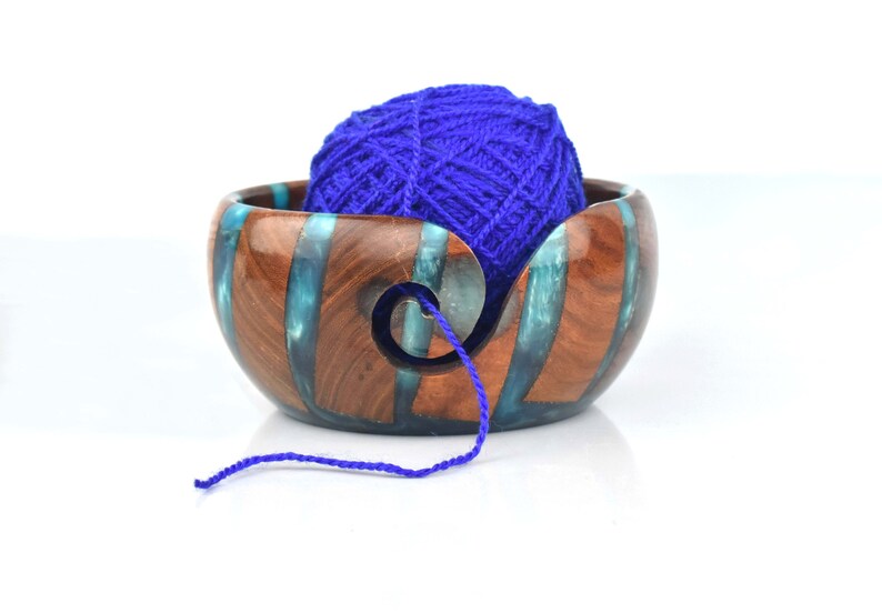 Pu&ograve; includere: Una ciotola per lana rotonda realizzata con segmenti di legno marrone scuro e resina traslucida color verde acqua. La ciotola presenta un intaglio a spirale sul lato anteriore per far passare il filo e contiene un gomitolo di lana blu reale.