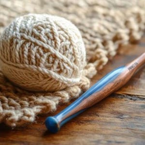 Pu&ograve; includere: Un gomitolo di lana color crema con un motivo a maglia testurizzato e un uncinetto con manico in legno lucido e inserto in resina blu, chiaramente contrassegnato con la misura 10.0MM, poggiato vicino a un pezzo di tessuto a maglia abbinato.