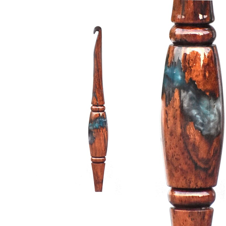 Puede incluir: Un ganchillo artesanal con mango de madera marr&oacute;n oscuro pulido con acabado brillante y una incrustaci&oacute;n central de resina azul y gris. La herramienta presenta una punta c&oacute;nica y una secci&oacute;n de agarre redondeada con detalles torneados.