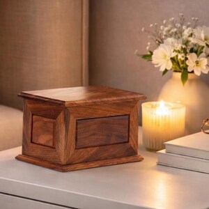 May include: A rectangular wooden box with a rich brown grain, featuring a flat lid and a beveled frame design on the front and side panels. The box has a smooth, polished finish and sits as a standalone object with a solid, structured appearance.