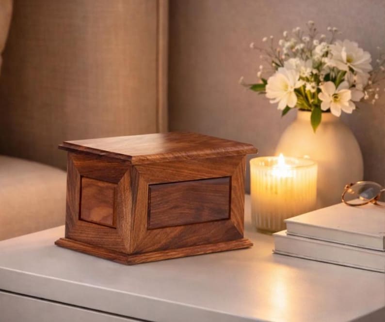 May include: A rectangular wooden box with a rich brown grain, featuring a flat lid and a beveled frame design on the front and side panels. The box has a smooth, polished finish and sits as a standalone object with a solid, structured appearance.
