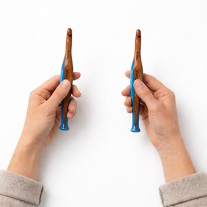 Pu&ograve; includere: Due uncinetti con un fusto in legno marrone e un manico ergonomico blu brillante. Gli uncinetti hanno una punta metallica e il marchio Tulip &egrave; stampato in bianco sulla parte blu del manico, insieme alle indicazioni delle dimensioni.