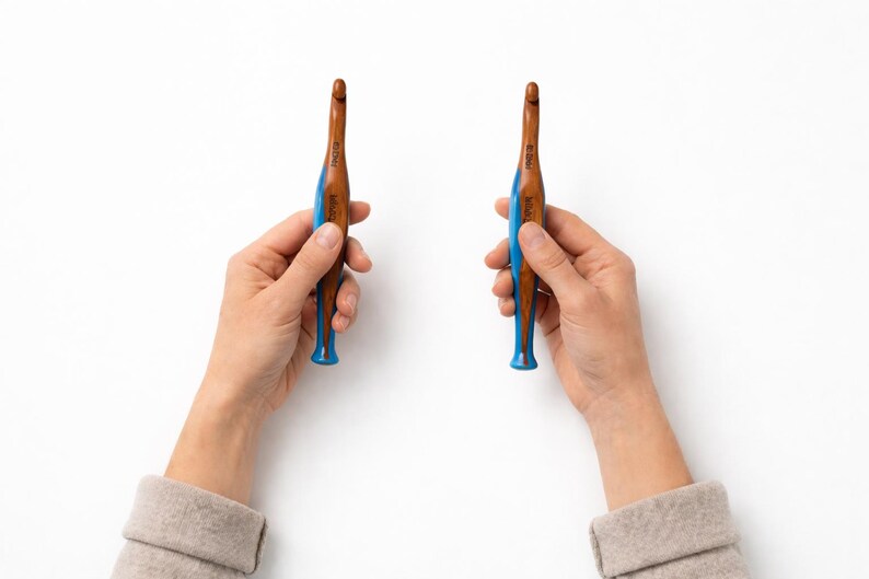 Pu&ograve; includere: Due uncinetti con un fusto in legno marrone e un manico ergonomico blu brillante. Gli uncinetti hanno una punta metallica e il marchio Tulip &egrave; stampato in bianco sulla parte blu del manico, insieme alle indicazioni delle dimensioni.