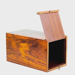 May include: A rectangular wooden box with a hinged lid, partially open. The box is made of a dark, richly grained wood with a warm, reddish-brown hue. The interior is black.