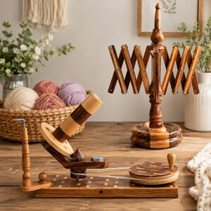 May include: A wooden yarn ball winder with a hand crank and a belt drive mechanism, positioned next to a wooden yarn swift. The winder features a light and dark wood finish, a central spool, and a circular base with a small handle for manual operation.