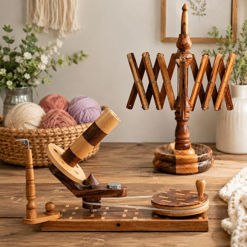 May include: A wooden yarn ball winder with a hand crank and a belt drive mechanism, positioned next to a wooden yarn swift. The winder features a light and dark wood finish, a central spool, and a circular base with a small handle for manual operation.